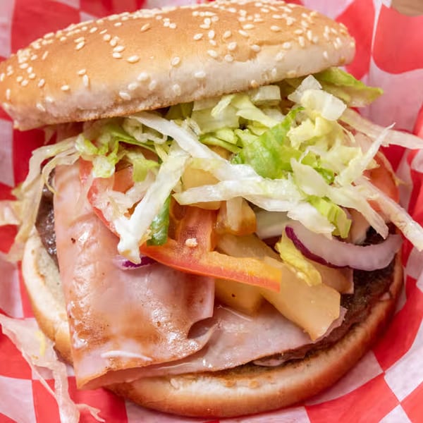 A large burger with ham, lettuce, tomatoes, onions, and fries on a sesame seed bun.