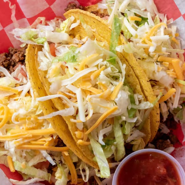 Three hard-shell tacos filled with ground beef, shredded lettuce, and cheddar cheese, with salsa.