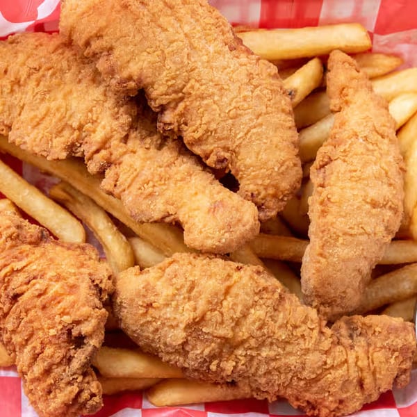Golden-brown fried chicken tenders and French fries in a red and white checkered paper basket.