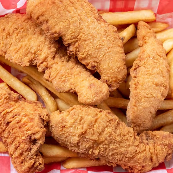 Close-up of golden-brown fried chicken tenders and french fries in a red and white checkered basket.