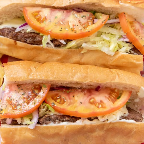 Two Giovanni's Pizza subs with meat, cheese, lettuce, onions, and tomatoes on a red and white checkered background.