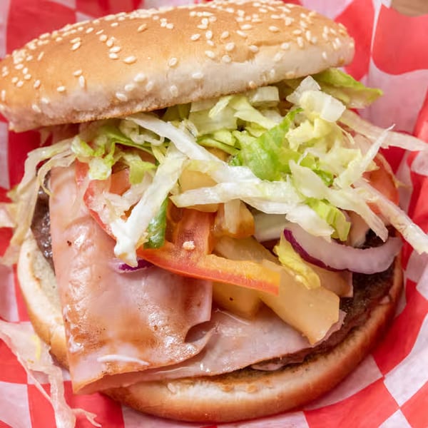 A close-up of a hamburger with ham, lettuce, tomatoes, onions, and fries in a red and white checkered wrapper.